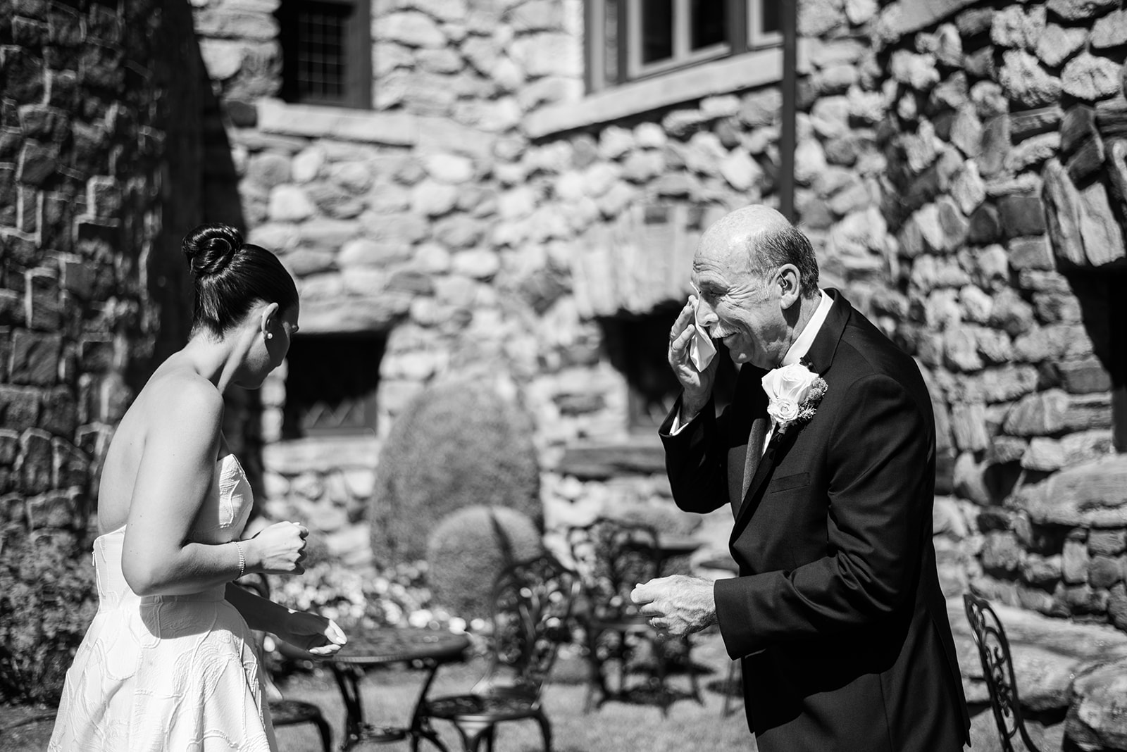 Black and white film photo of the father wiping away a tear during an emotional first look with the bride.